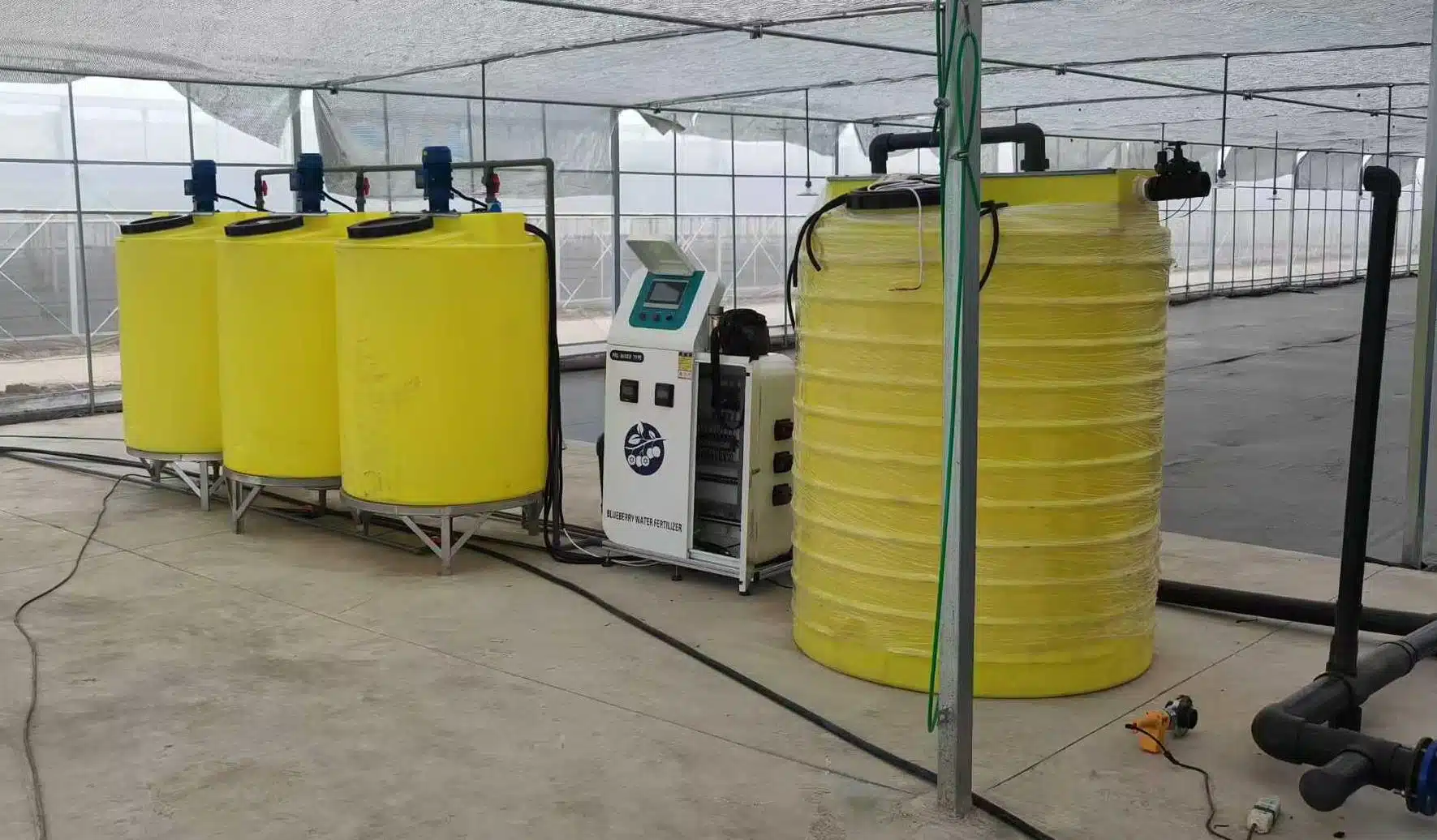 Automated fertigation system in greenhouse with yellow nutrient tanks and control panel
